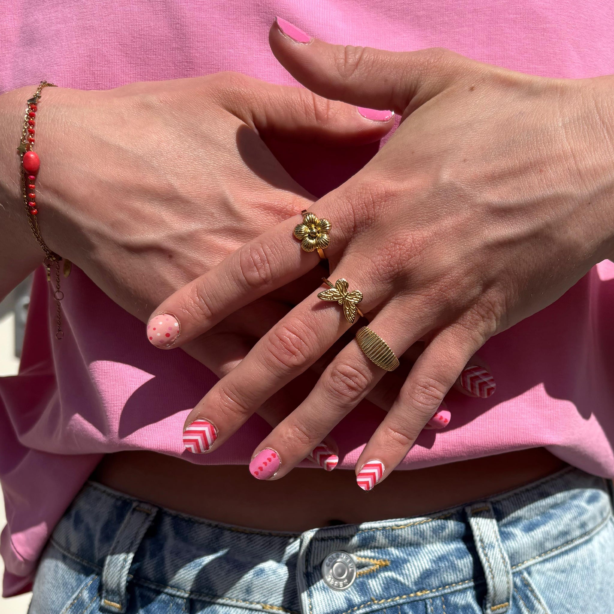 twee handen met gouden ringen laten nagelstickers met roze figuurtjes zien