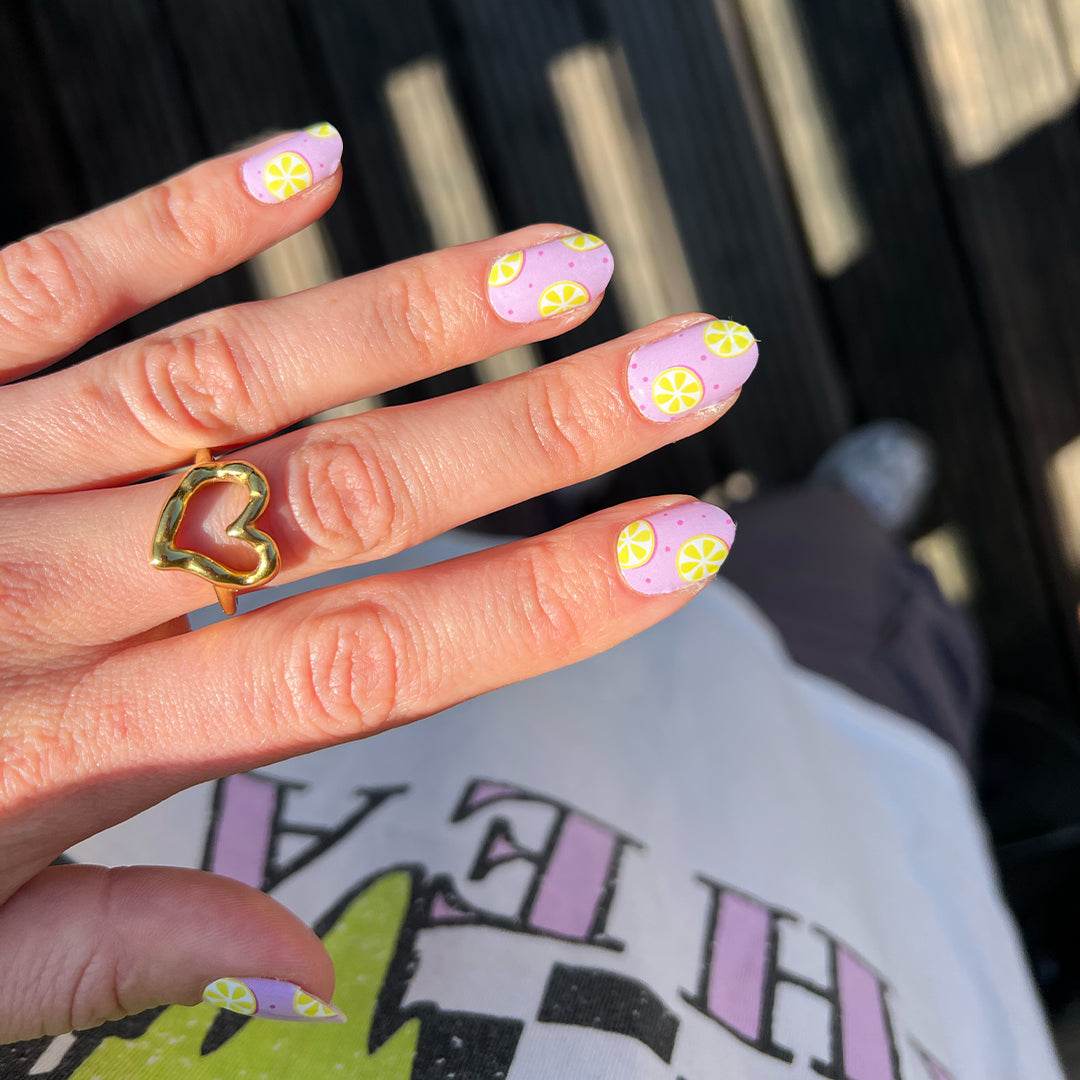 Hand laat nagelstickers met lila en gele citroenen zien