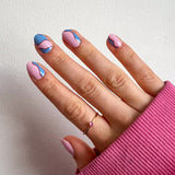 Hand laat nagelstickers met roze en blauwe print zien met roze mouw en witte achtergrond