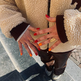 twee handen laten nagelstickers in rood en oranje zien met teddy vest en gouden ringen