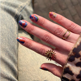 Hand laat nagelstickers met gekleurde swirls en daisybloemen zien met gouden ringen