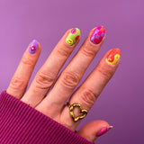 Hand met roze trui laat nagelstickers zien met paarse, roze en groene 70's hippie patroon op paarse achtergrond