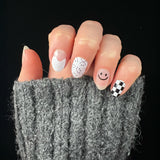 Hand met grijze wollige trui laat zwart-witte nagelstickers zien met smileys en blokjes
