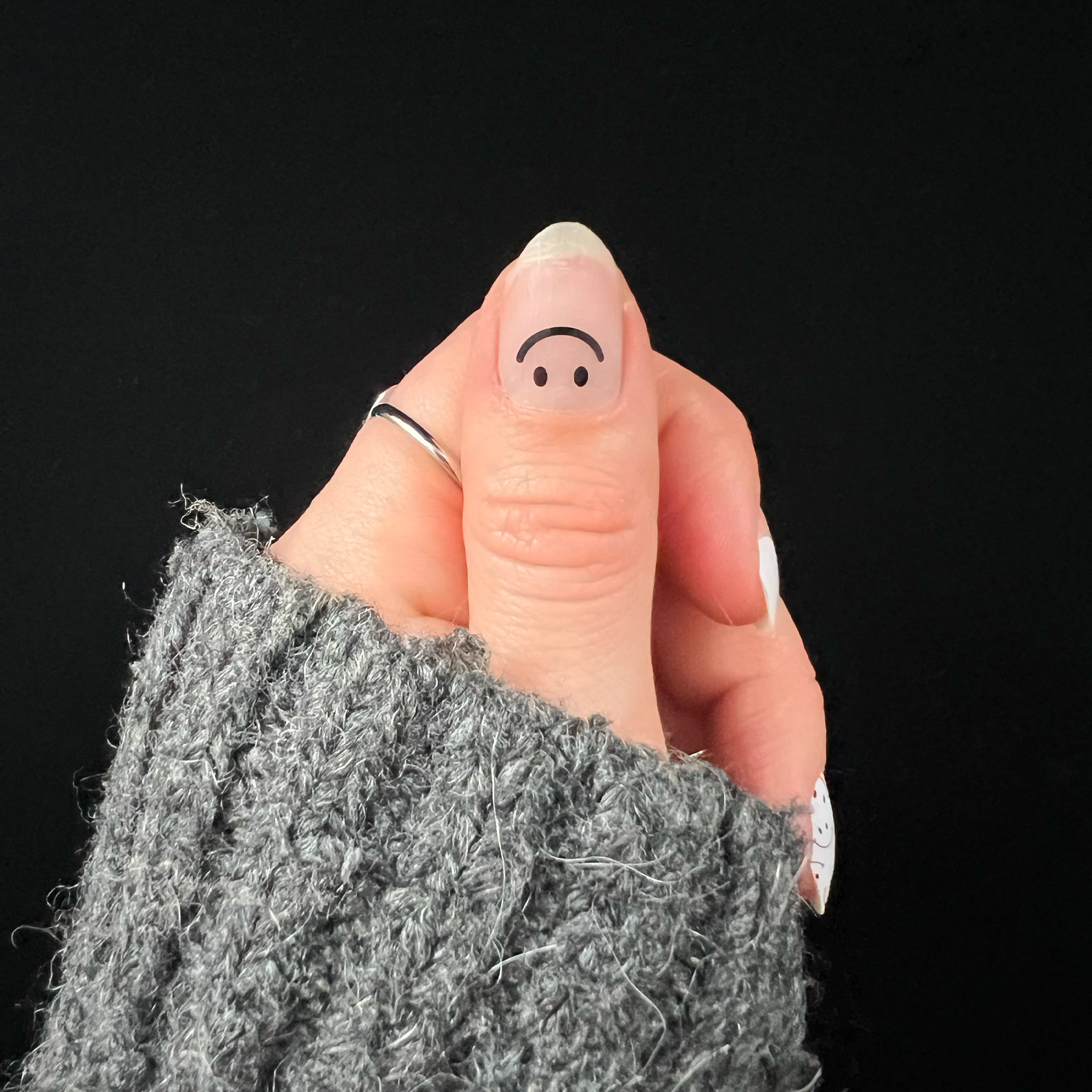 Hand met grijze wollige trui laat duim met nagelsticker met zwarte smiley zien