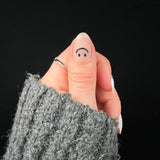 Hand met grijze wollige trui laat duim met nagelsticker met zwarte smiley zien