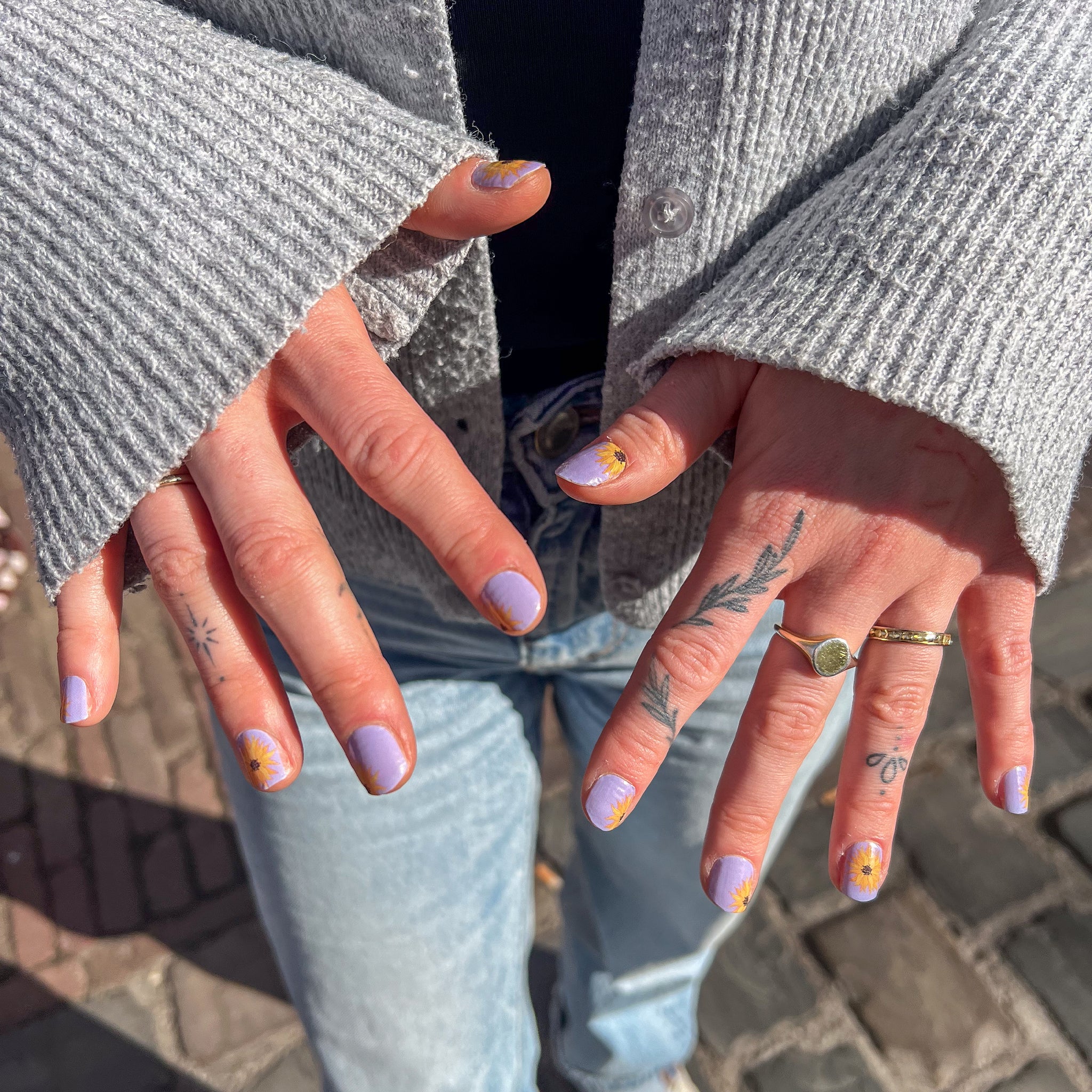handen laten gouden ringen met paarse nagelstickers zien met een zonnebloem