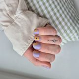 hand laat paarse nagelstickers zien met een zonnebloem op witte achtergrond met groene ruitjes broek