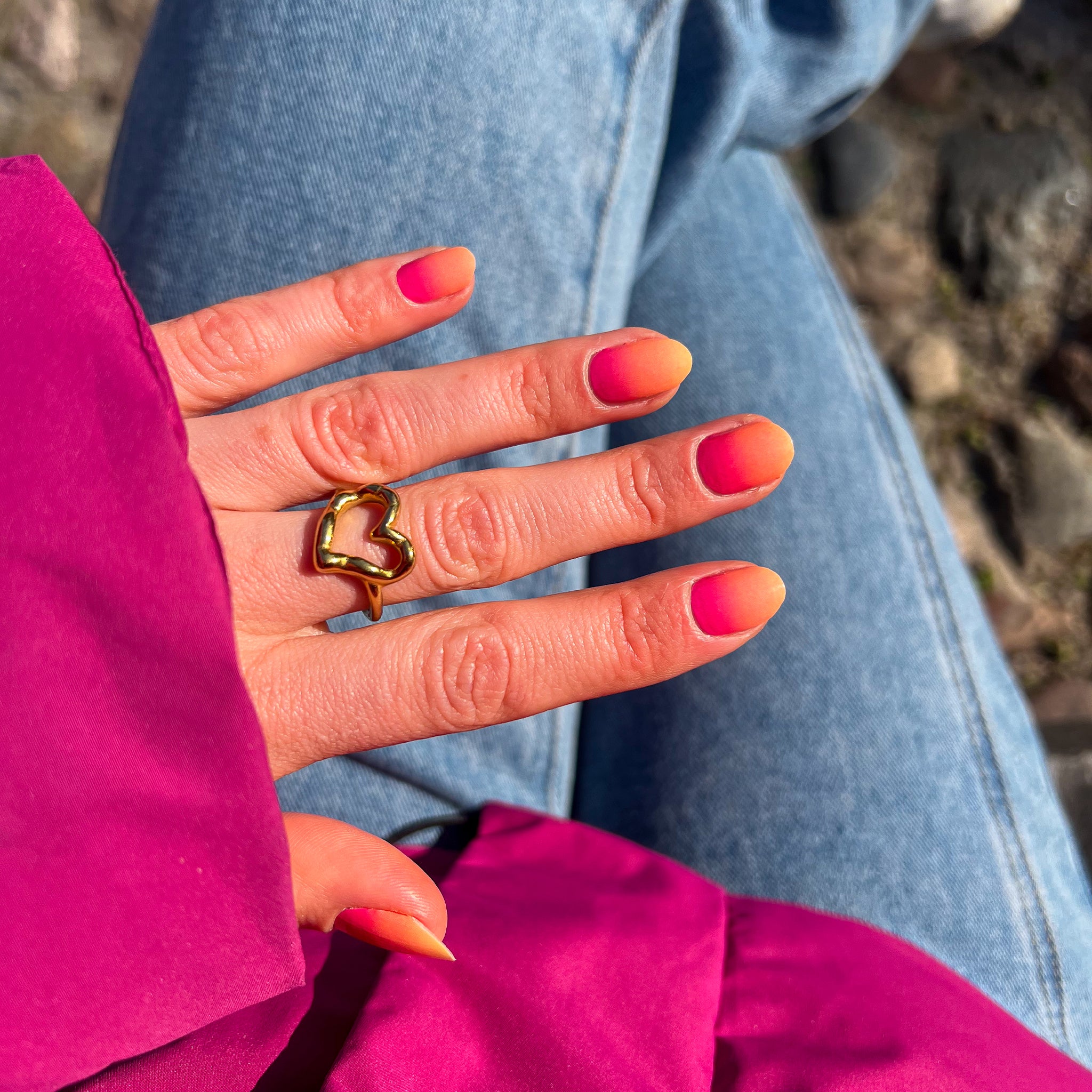Hand laat nagelstickers met rood-roze verloop zien met roze winterjas en blauwe jeans