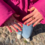 twee handen laten nagelstickers met rood-gele gradient zien en roze winterjas met blauwe jeans