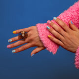 2 handen tonen nagelstickers op nagels met een mix van roze, groen, blauw, geel en bloemenpatroon