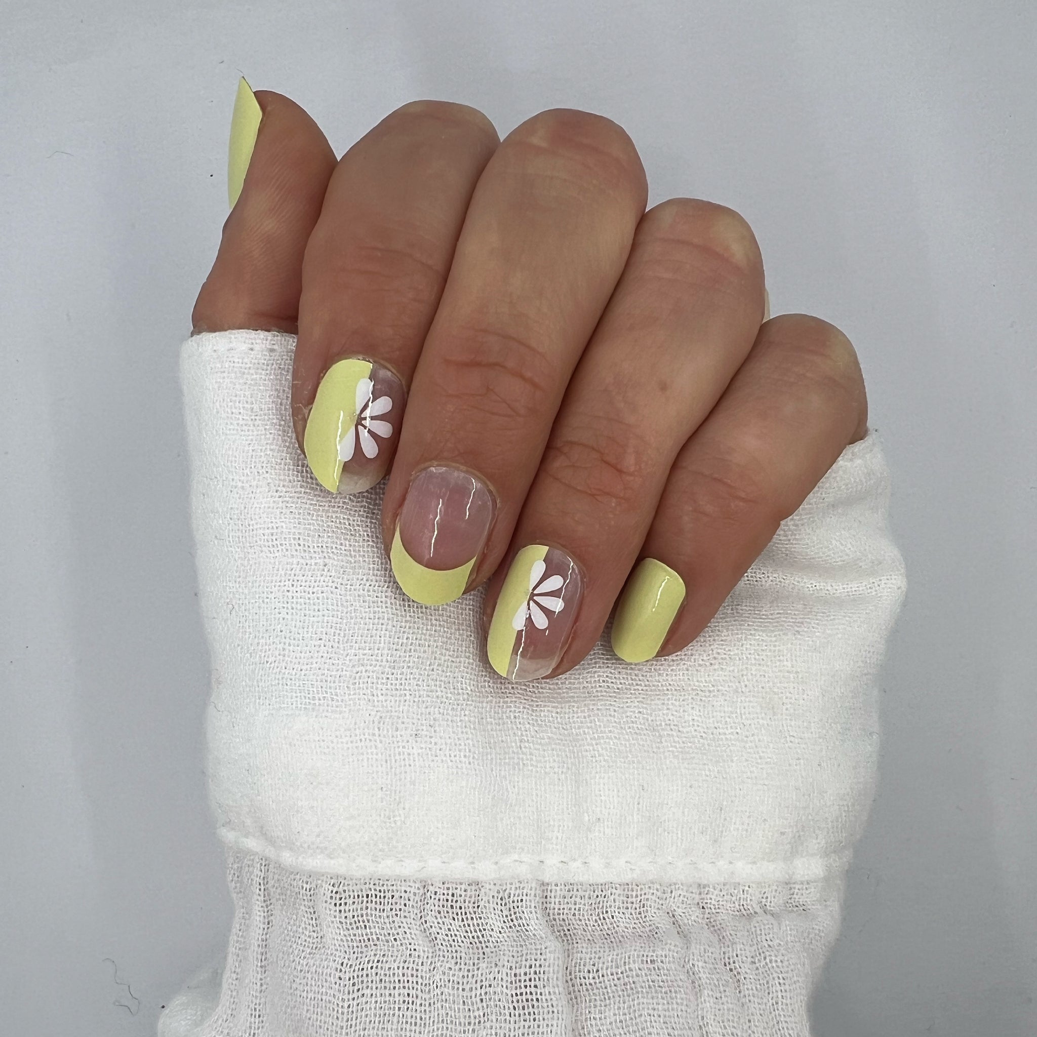 Hand laat butter yellow nagelstickers zien op witte achtergrond met witte blouse
