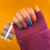 Nagels laten nagelstickers zien met kleurrijke hartjes op gele achtergrond en met donkerroze mouw