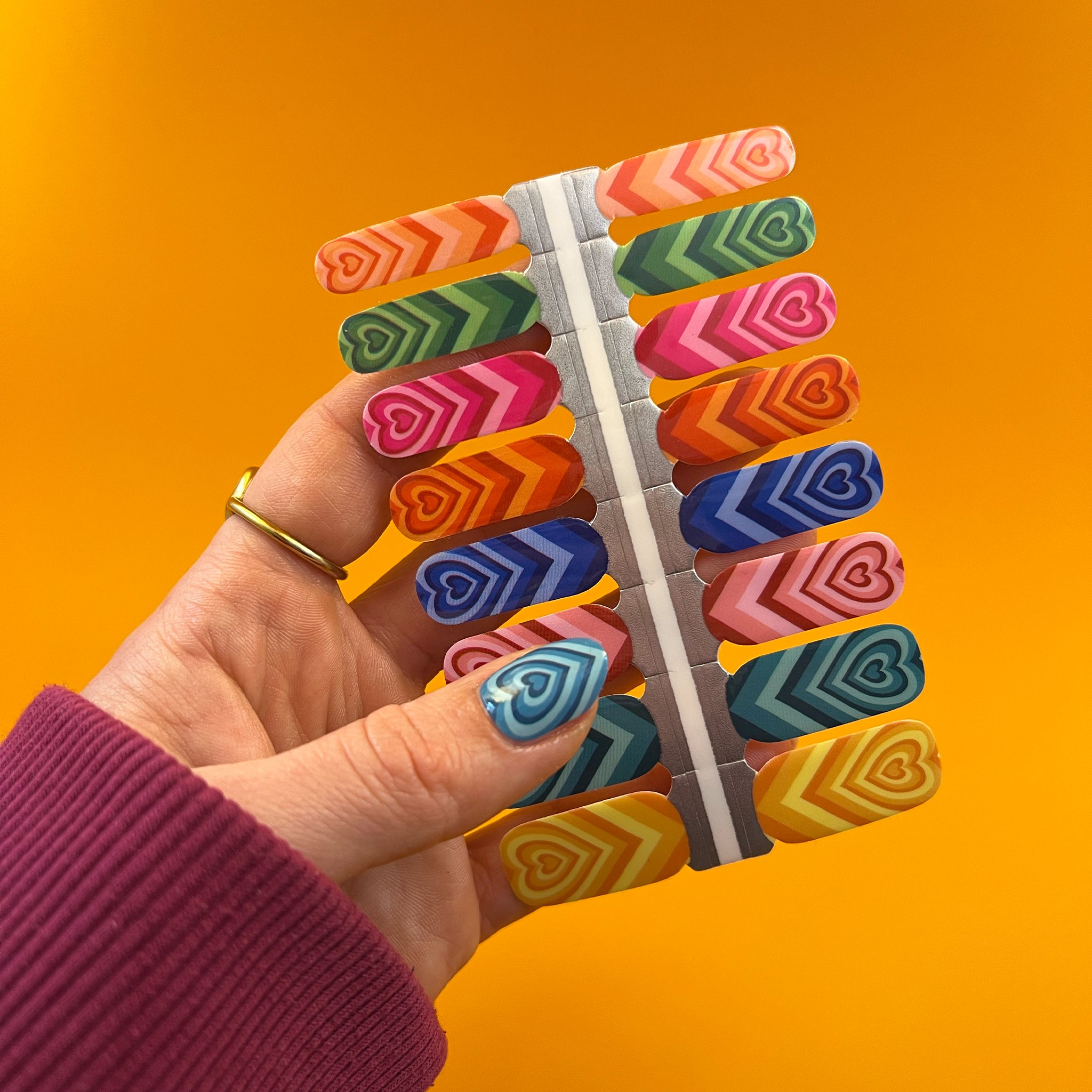 Hand houdt nagelstickers met kleurrijke hartjes vast boven gele achtergrond