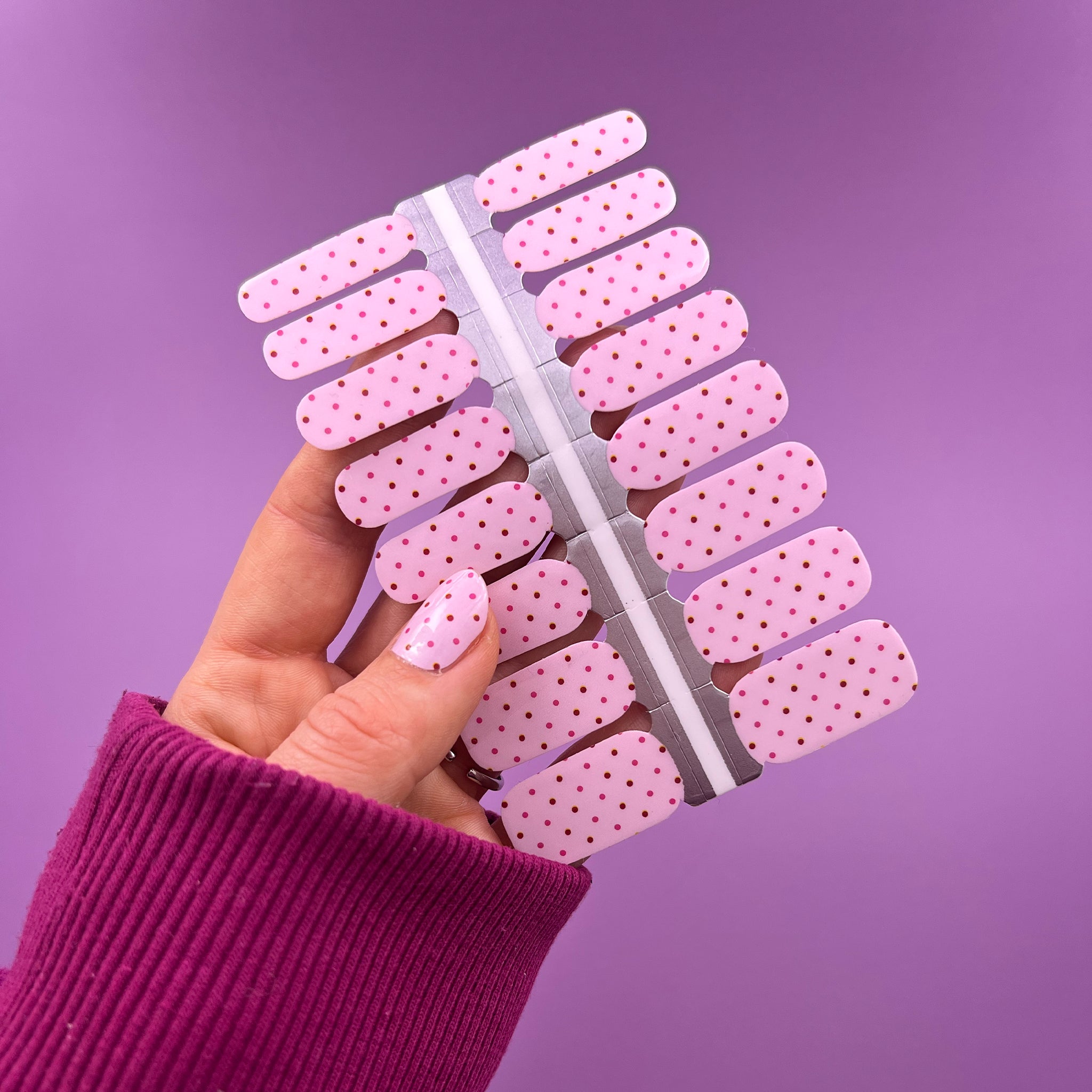 Hand laat nagelstickers zien met lichtroze rode en roze stipjes op paarse achtergrond