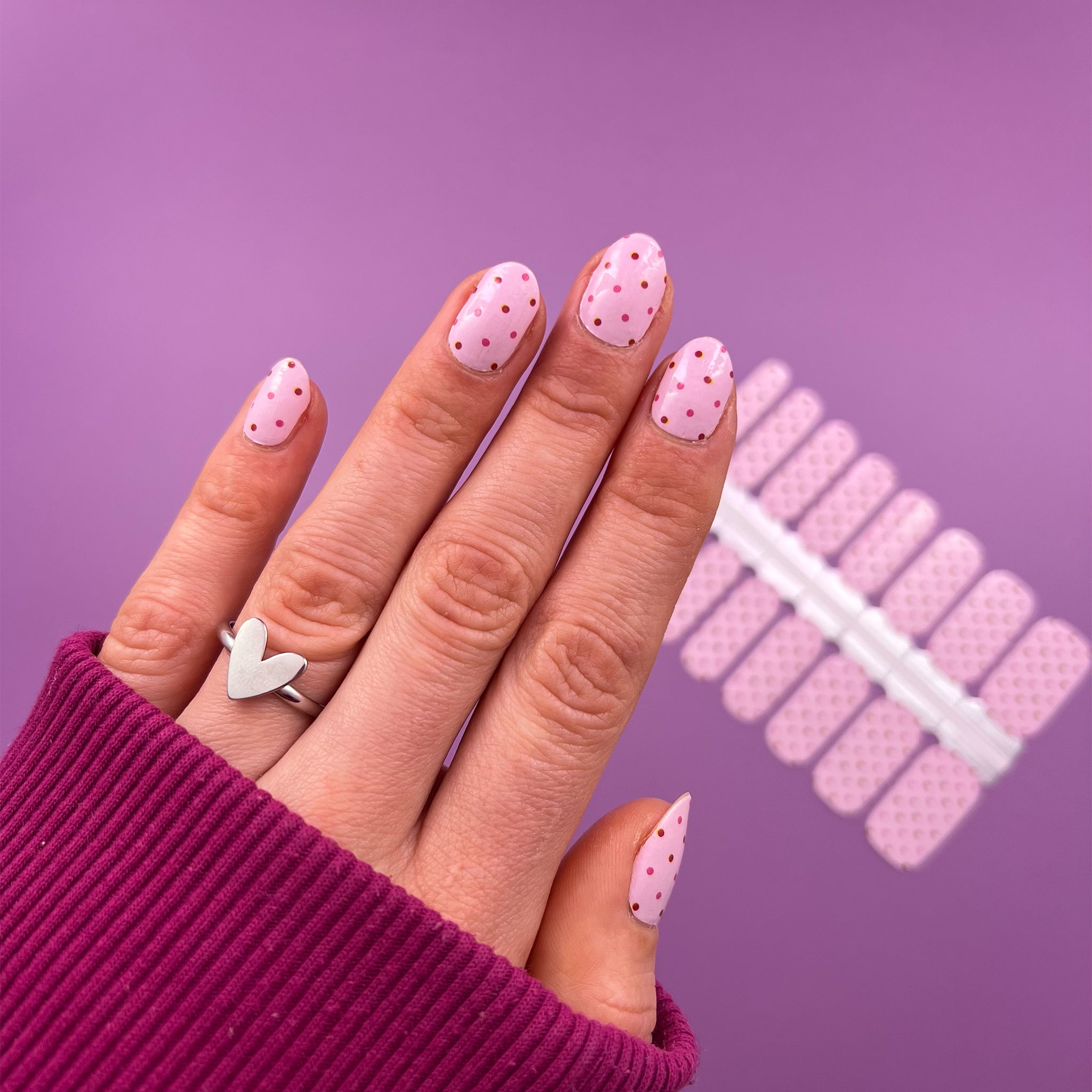 Hand laat nagelstickers zien met lichtroze rode en roze stipjes op paarse achtergrond
