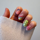 Hand met witte trui met nagelstickers met felle kleuren in funky en groovy stijl