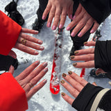 6 handen laten nagelstickers zien in een cirkel op een ondergrond van sneeuw