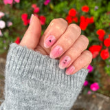 Hand laat roze nagelstickers met aura ring zien met zwart strikje met een ondergrond van rode bloemen