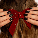 Twee handen met zwarte glitter nagelstickers doen donkerrode strik vast in bruin haar