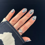 Hand laat nagelstickers zien met zwart-witte zebraprint op zwarte achtergrond