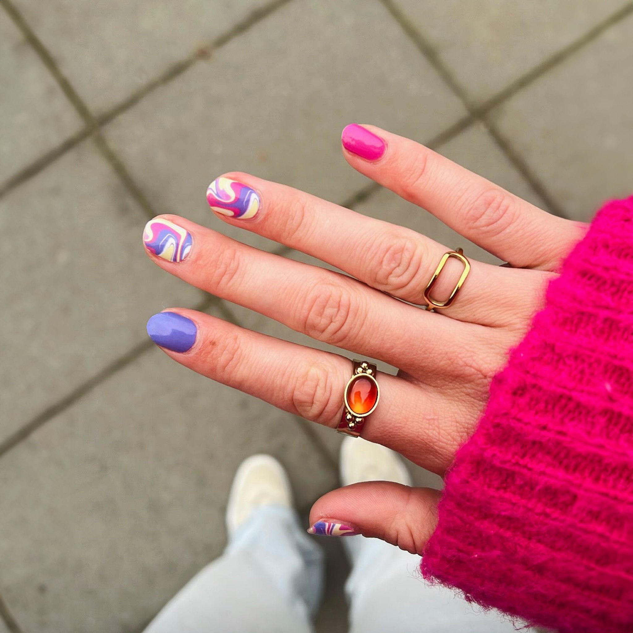 Hand laat nagelstickers zien met gekleurde marmer en roze trui