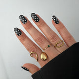 Hand met gouden ringen laat zwarte nagelstickers met witte stippen zien