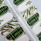 Detailfoto van nagelstickers met groene slangenprint op witte achtergrond