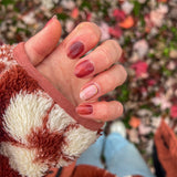 Hand toont bruine nagelstickers met gouden randje op een ondergrond van bladeren en bloemen vest