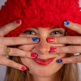 Model kijkt in camera met vingers voor gezicht die nagelstickers met roze, rode en blauwe met vrolijke patronen tonen