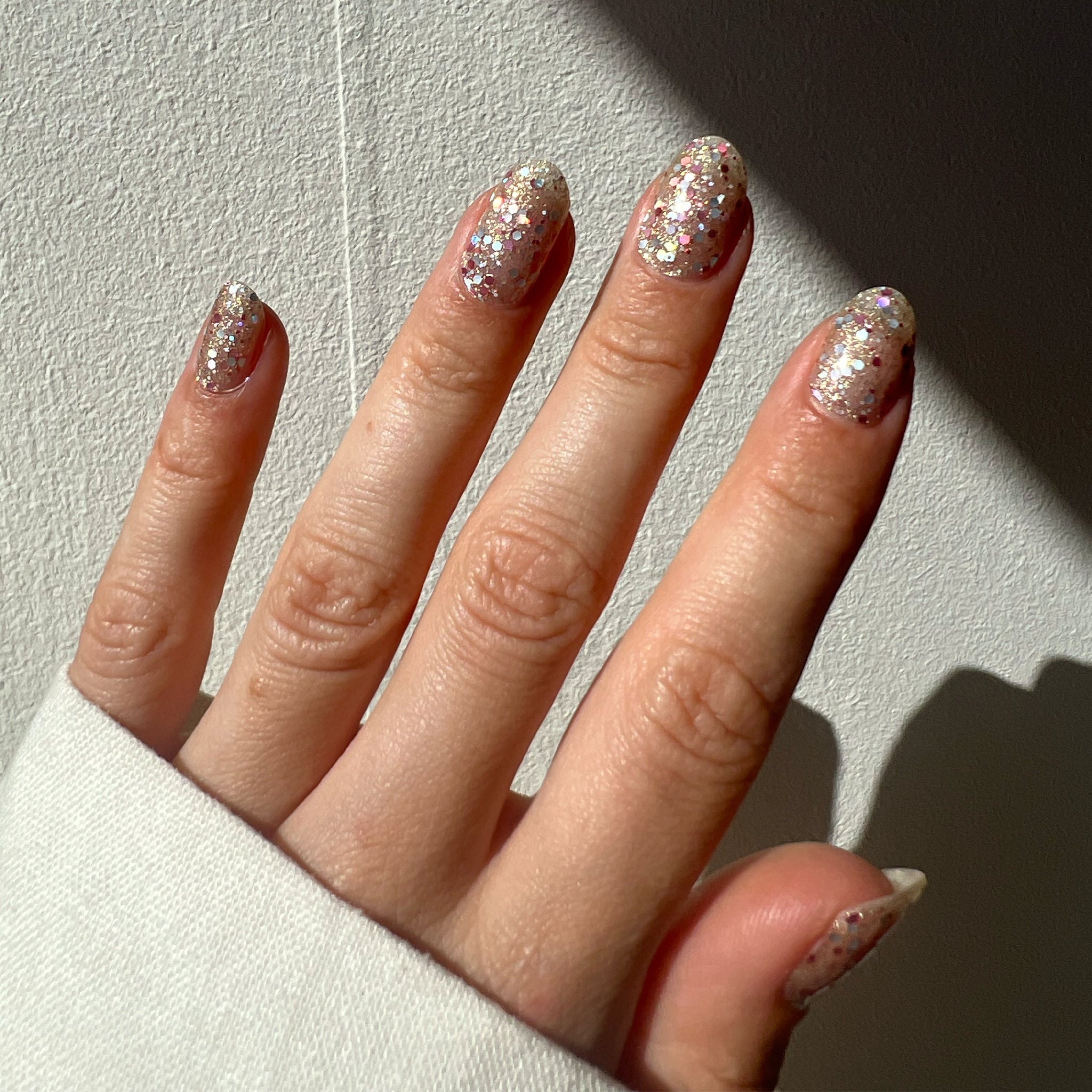 Hand toont nagelstickers met gouden glitters en gekleurde pailletten