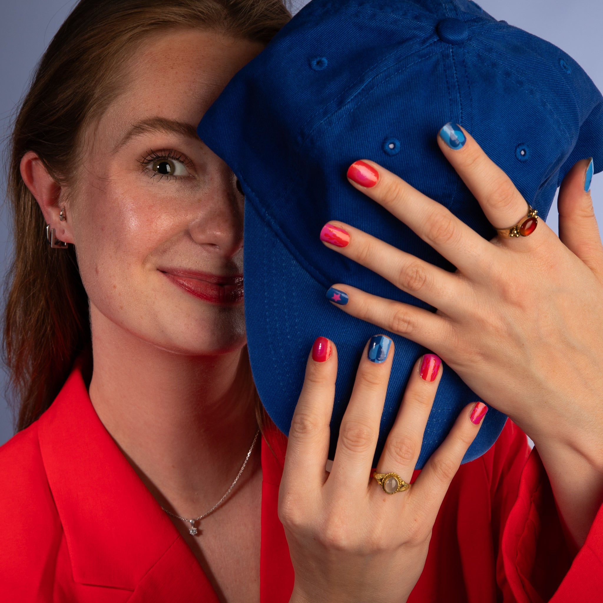 Model houdt blauwe pet vast en toont nagelstickers met roze, rode en blauwe met vrolijke patronen