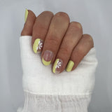 Hand laat butter yellow nagelstickers zien op witte achtergrond met witte blouse