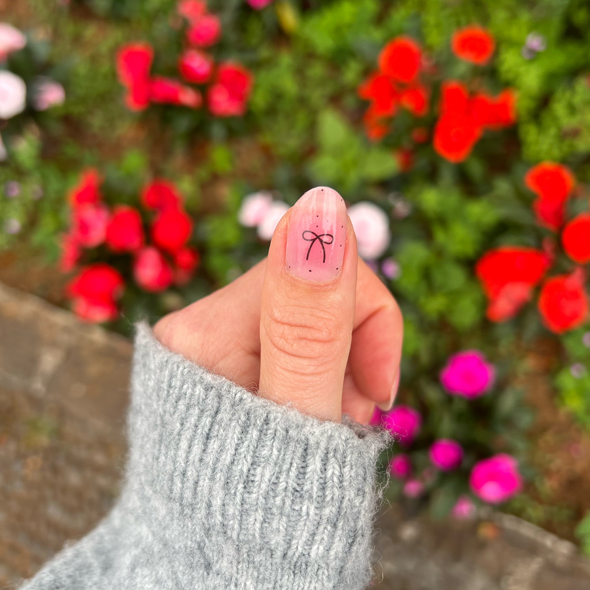 Duim laat roze nagelsticker op nagel zien met zwart strikje met een ondergrond van rode bloemen