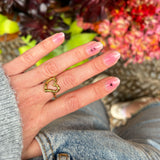 Hand laat roze nagelstickers met aura ring zien met zwart strikje met een ondergrond van rode bloemen