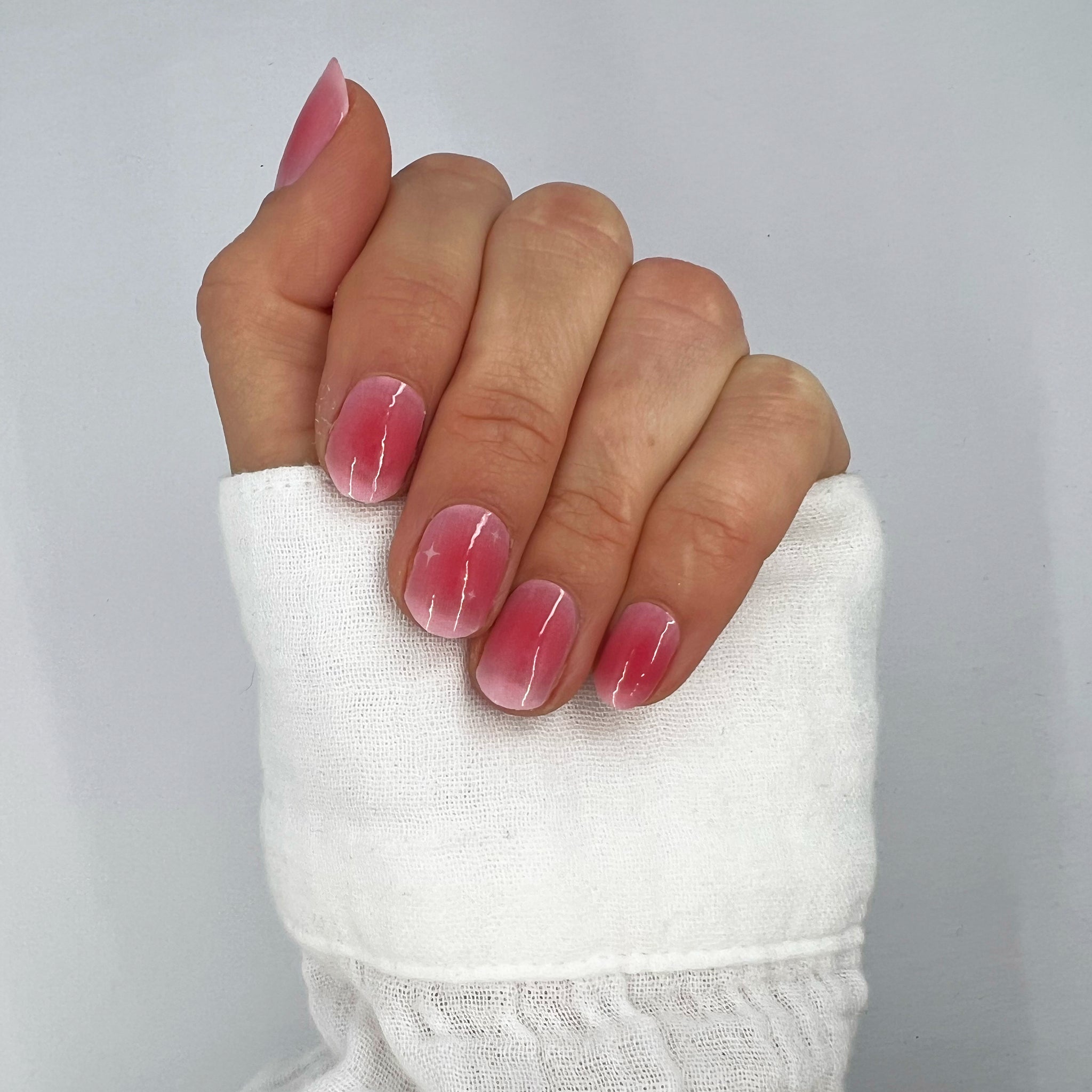 Hand met witte blouse laat nagelstickers zien met roze aura en witte twinkels op witte achtergrond