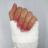 Hand met witte blouse laat nagelstickers zien met roze aura en witte twinkels op witte achtergrond
