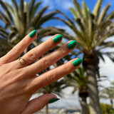 Hand met groene glitter nagelstickers met palmbomen in achtergrond en blauwe lucht