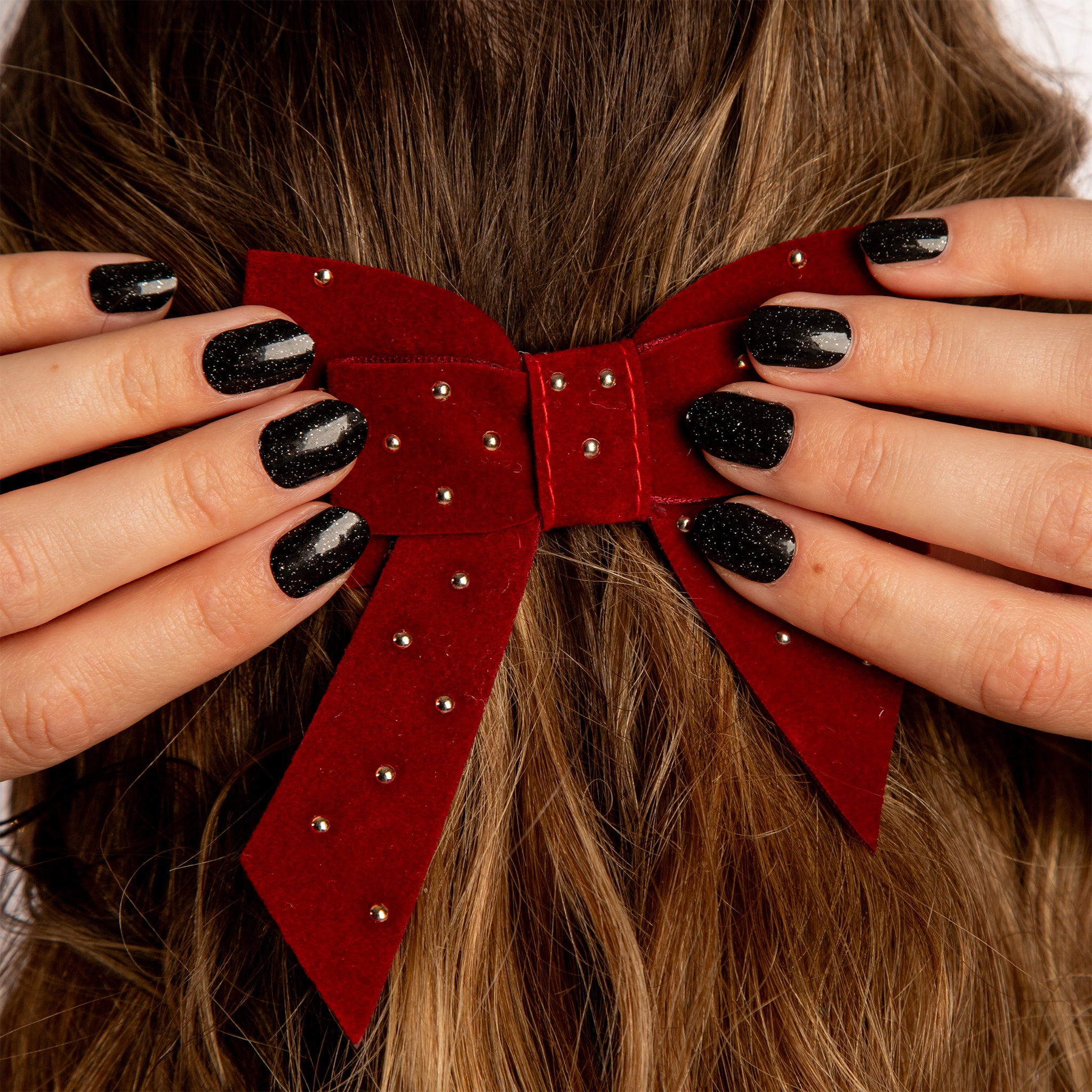 Twee handen met zwarte glitter nagelstickers doen donkerrode strik vast in bruin haar
