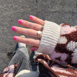 hand met wollen trui en ringen laat roze met paarse nagels zien