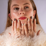 Model met beige bontjas toont handen met nagelstickers met bruine en beige met lijnen