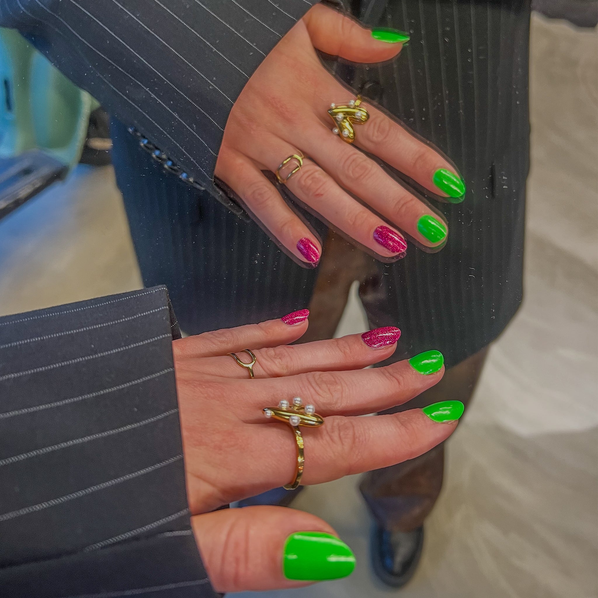 Hand in spiegel met ringen en groene en roze nagelstickers