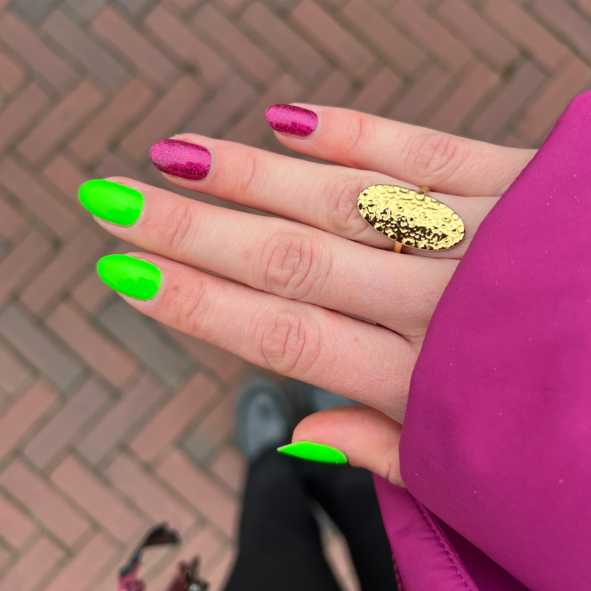 Hand met groene en roze nagellak met roze jas en gouden ring