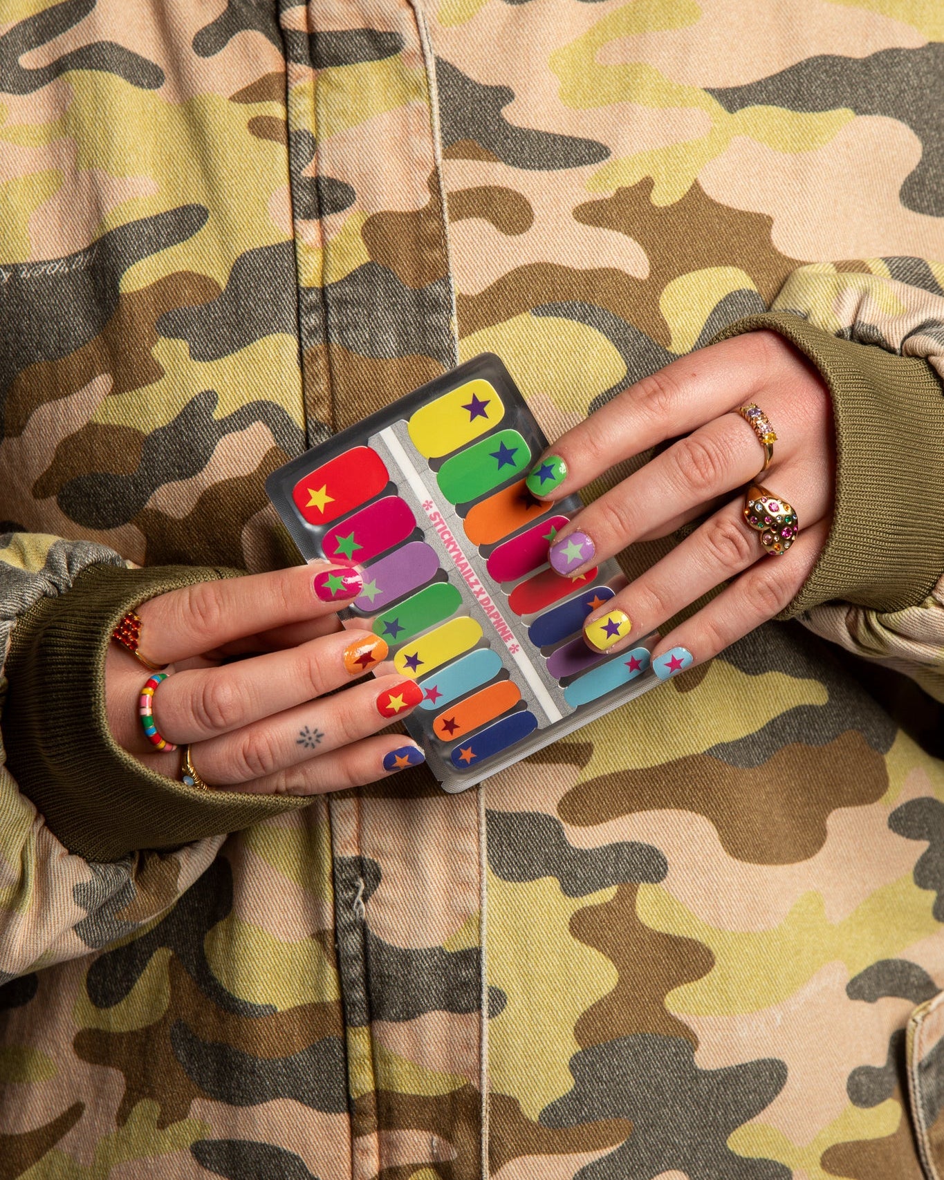 twee handen houden nagelsticker met kleuren en sterren vast met camouflage jasje