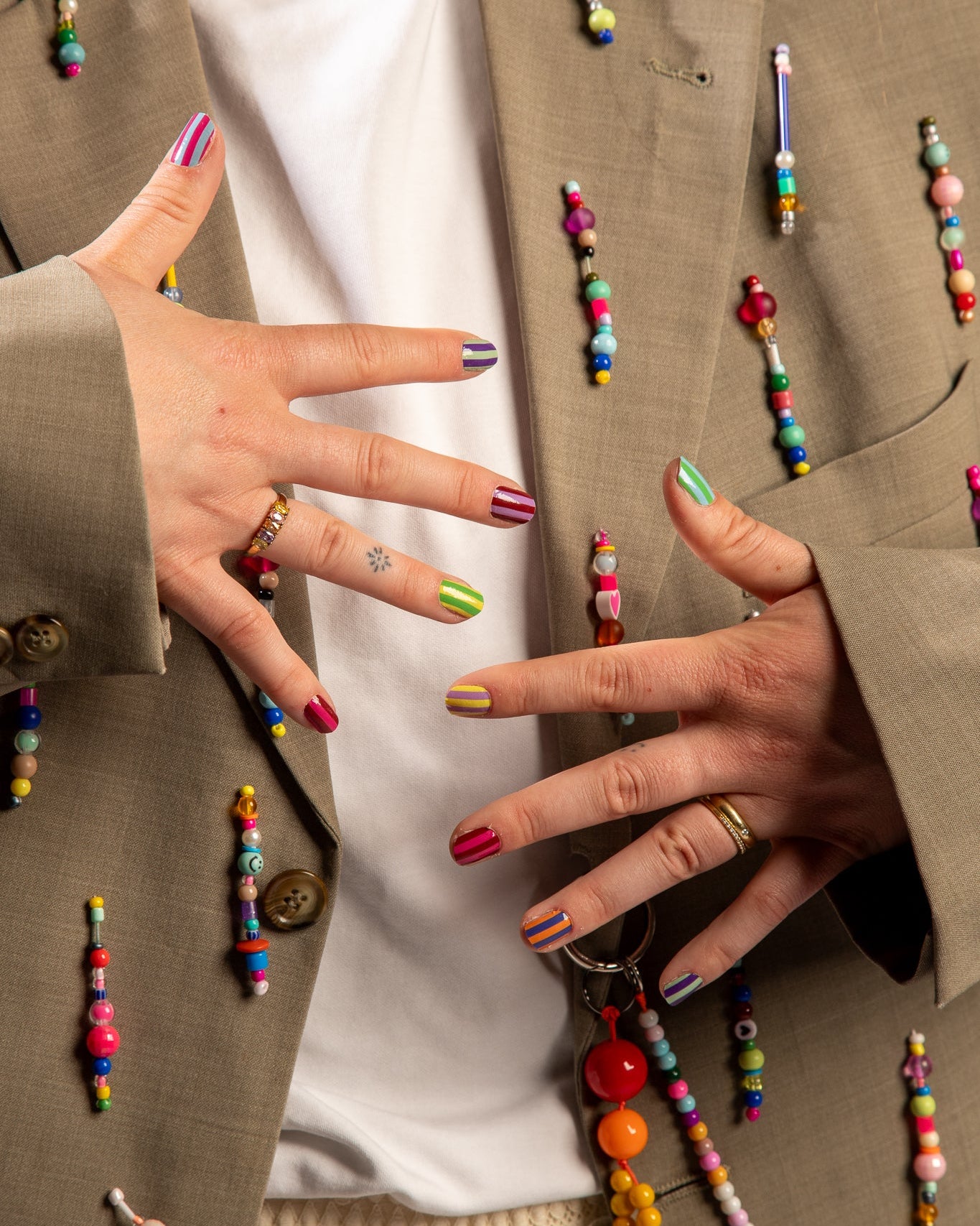 Twee handen laten nagels zien met blazer en kleurrijke kralen