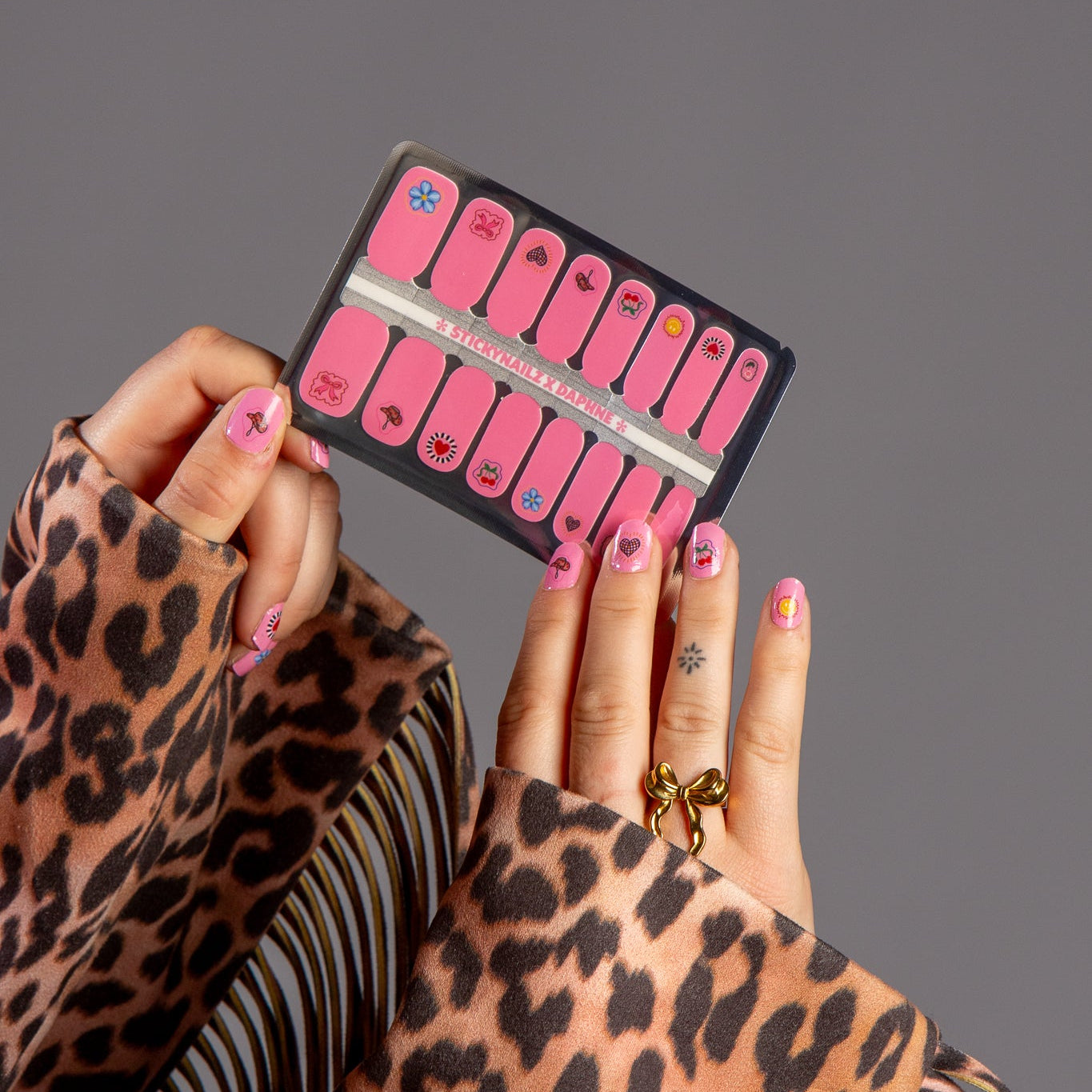 handen laten nagelstickers zien met roze iconen en panterprint jas met franjes